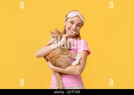 Belle femme mûre avec chat mignon se brossant les dents sur fond jaune Banque D'Images