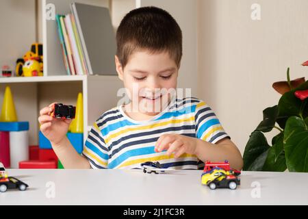 Un enfant d'âge préscolaire joue avec des voitures jouets assises à une table à la maison. Banque D'Images