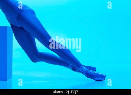 Gros plan ballerine jambes fines dans des chaussures pointe isolées sur fond bleu marine studio de couleur au néon. Art, mouvement, action, flexibilité, inspiration Banque D'Images