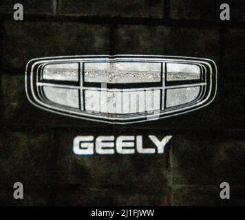 Minsk, Biélorussie-mars 2022 : un emblème de voiture Geely brillant sur un carreau de béton. Photo de nuit dans l'obscurité. Photo horizontale. Banque D'Images