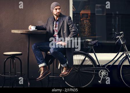 Le café est toujours une bonne idée. Photo d'un beau jeune homme en tenue d'hiver ayant une boisson dans un café-terrasse. Banque D'Images