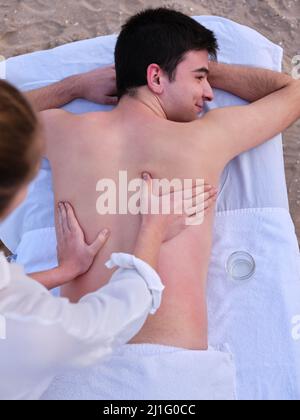 Un jeune homme détendu recevant un chiromassage par un chiromassage thérapeute sur une plage de Valence. Banque D'Images