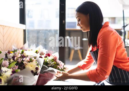 Vue latérale de jeune femme Barista caucasien touchant le bouquet de fleurs fraîches au café-restaurant. Non modifié, culture de café, les gens et l'occupation concept. Banque D'Images