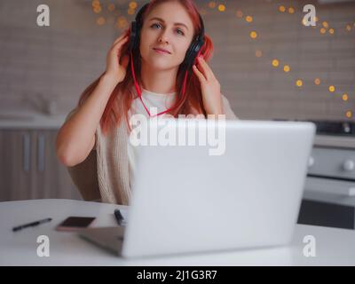 jeune femme attrayante travaillant avec un ordinateur portable dans la cuisine. femme décontractée appréciant sa chanson préférée sur un casque et chantant tout en travaillant sur un ordinateur portable dans le bureau à la maison. Banque D'Images