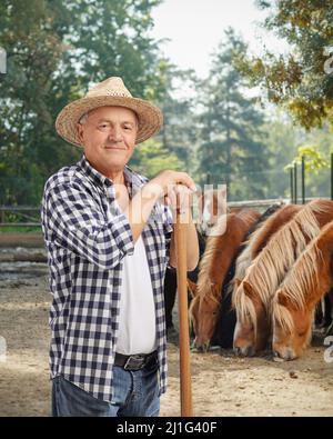 Agriculteur mature avec une pelle posant avec des chevaux à l'arrière Banque D'Images