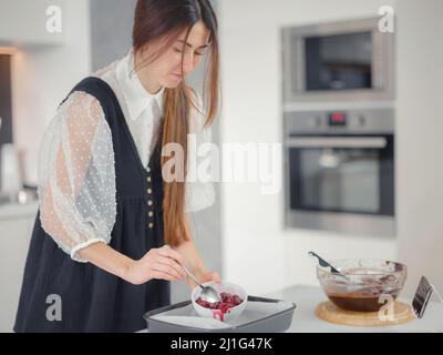 concept de boulangerie, de nourriture et de personnes. Femme préparant le brownie au chocolat à la table de cuisine, gros plan. La cuisinière met les cerises dans le sucre sur une plaque de cuisson Banque D'Images