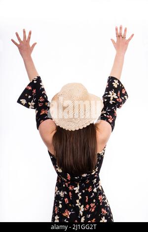 Jeune fille aux bras levés. La fille est photographiée de derrière, elle porte une robe noire à fleurs et un chapeau. Banque D'Images