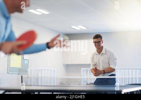 S'amuser au bureau. Coup de feu de deux jeunes hommes d'affaires jouant au tennis de table au travail. Banque D'Images