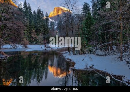 Half Dome illuminé par la lumière du coucher du soleil se reflète sur la rivière Merced en hiver, parc national de Yosemite Banque D'Images