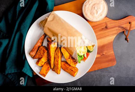 Emballage de légumes rôtis et de Halloumi servi avec des mèches de pommes de terre sucrées : enveloppement végétarien avec courgettes, poivrons rouges, arugula, champignons et oignons Banque D'Images