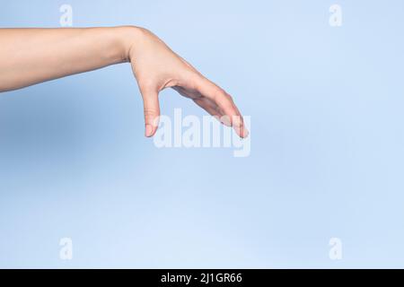 Femme geste de main. La main femelle pose comme tenir ou cueillir quelque chose d'isolé sur fond bleu clair. Vue avant Banque D'Images