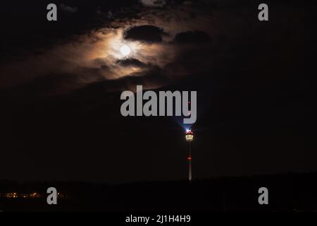 Tour de télévision de Stuttgart la nuit, pleine lune qui brille à travers le ciel nuageux, marqueurs de position rouges et faisceau lumineux lumineux lumineux Banque D'Images