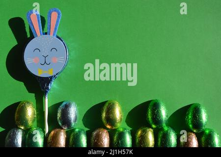 Lapin de Pâques et œufs enveloppés de papier d'aluminium au chocolat sur fond vert vif avec espace de copie Banque D'Images