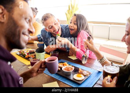 Groupe d'amis déjeuner au restaurant. Des jeunes joyeux mangent des hamburgers et apprécient un restaurant de restauration rapide. Banque D'Images