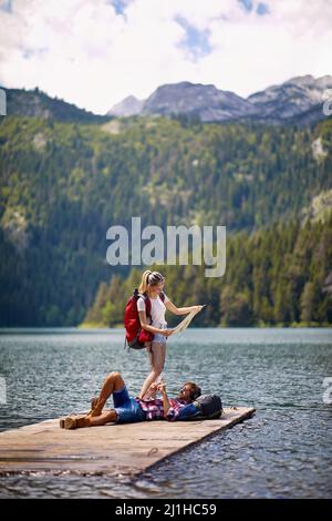 Jeune couple avec des sacs de tabac à l'aventure. Homme allongé sur une jetée en bois au bord du lac, femme regardant la carte. Concept de style de vie, de convivialité, de nature Banque D'Images