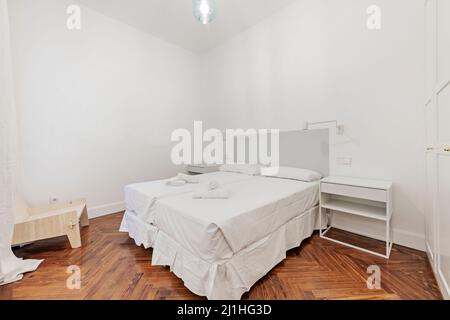 Chambre avec lits doubles et draps blancs, serviettes de bain sur les lits, tables de chevet blanches et parquet en pin Banque D'Images