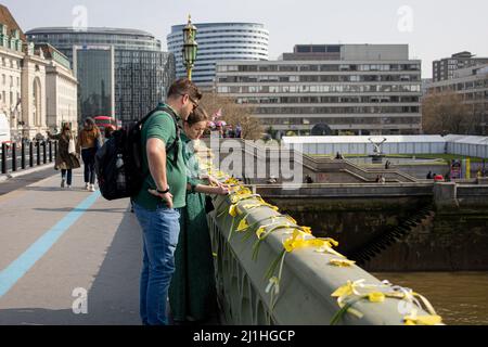 Londres, Royaume-Uni. 25th mars 2022. Deux piétons sont vus lire le message sur les rubans jaunes du pont de Westminster. La Journée nationale de réflexion a eu lieu le 23rd mars 2022, le deuxième anniversaire du confinement en 1st au Royaume-Uni en raison de la COVID-19, pour rappeler les vies perdues pendant la pandémie de Covid-19. Crédit : SOPA Images Limited/Alamy Live News Banque D'Images