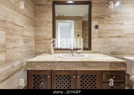 Salle de bains avec murs carrelés de marbre, miroir encadré en bois et meuble-lavabo en marbre avec évier en porcelaine blanche Banque D'Images