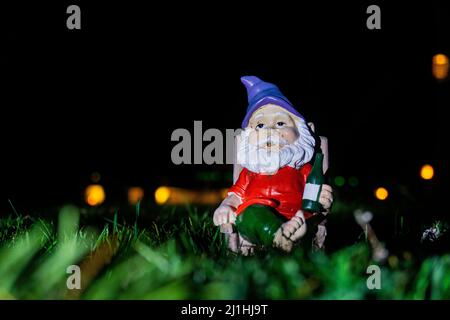 Gnome de jardin en face de fond noir relaxant sur l'herbe verte au milieu de la nuit. Banque D'Images