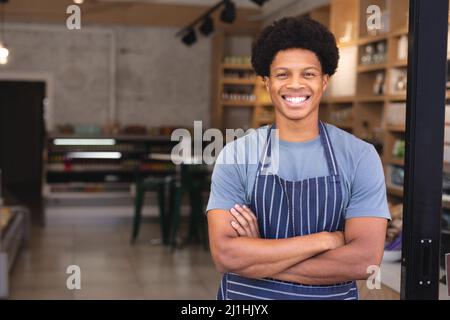 Portrait d'un jeune homme afro-américain heureux avec les bras croisés portant un tablier au café-restaurant. Non modifié, culture de café, les gens et l'occupation con Banque D'Images