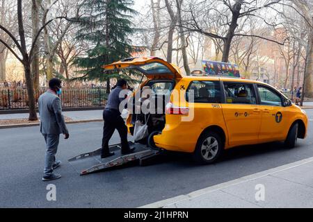 Un chauffeur de taxi New York aide un fauteuil roulant à se rendre dans un taxi jaune New York City avec une rampe accessible aux personnes à mobilité réduite à l'arrière. Banque D'Images