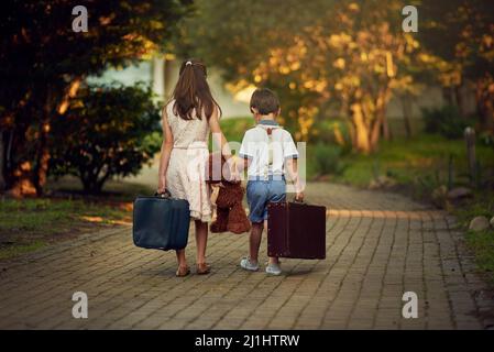 Tout est emballé et c'est parti. Photo d'une petite fille et de son frère qui s'éloignent tout en portant des valises et des jouets. Banque D'Images