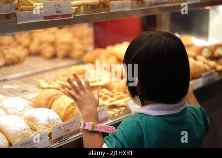 Jeunes filles clings à la boulangerie vitrine au marché de nuit thaïlandais, regardant thirstilly à de nombreux petits pains, tartes et muffins Banque D'Images