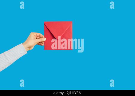 Main tenant une enveloppe rouge avec lettre, message ou avis sur fond bleu Banque D'Images