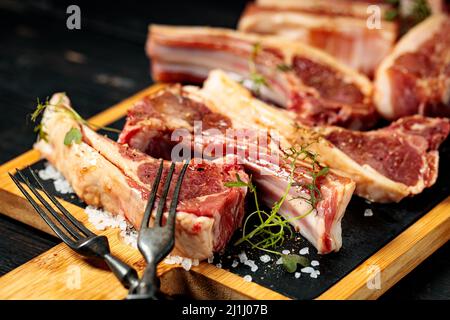 Steak brut en T et côtes sur une planche à découper en pierre noire. Viande crue aux épices et aux herbes. Gros plan. Arrière-plan en bois sombre. Banque D'Images