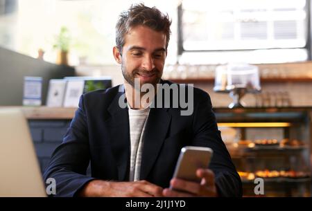 Il sait faire les choses. Photo d'un beau jeune homme utilisant un téléphone et un ordinateur portable dans un café. Banque D'Images