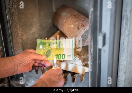 Ancien retraité tenant des billets de banque en main devant un poêle à bois et un briquet en bois dans un appartement, Allemagne Banque D'Images