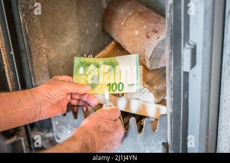 Ancien retraité tenant des billets de banque en main devant un poêle à bois et un briquet en bois dans un appartement, Allemagne Banque D'Images