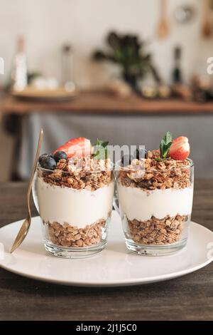 Gros plan de deux grandes tasses de granola verglassy décorées de baies placées sur une assiette avec une cuillère dorée dans la cuisine Banque D'Images