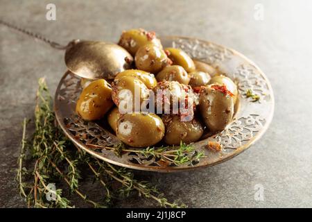 Olives vertes épicées à l'huile d'olive dans un ancien bol en métal.Bol avec olives et brindilles de thym sur une table en pierre. Banque D'Images