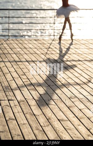 Ombre d'une danseuse de ballet féminine floue sur une jetée en bois ensoleillée Banque D'Images