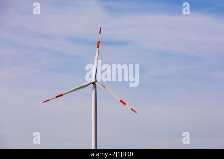 Une éolienne rouge et blanche à trois hélices contre le ciel bleu Banque D'Images