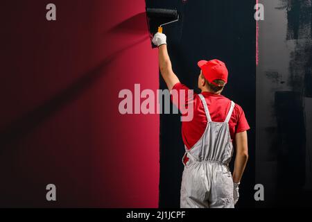 Homme peint un mur. Peintre en rouge mur de peinture en noir Banque D'Images