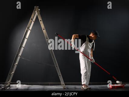 Homme peint un mur. Peintre en rouge mur de peinture en noir Banque D'Images