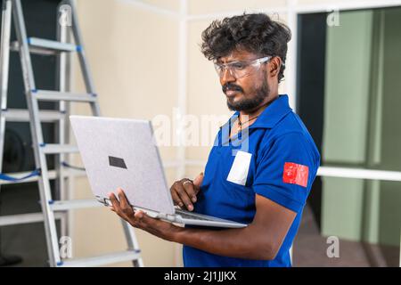 Ouvrier de partition en aluminium occupé à utiliser l'ordinateur portable sur le chantier - concept de la technologie, de rénovation et de service d'entretien. Banque D'Images