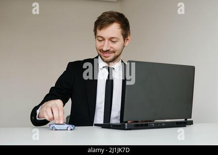 Jeune homme d'affaires en costume jouant avec une petite voiture sur la table dans son bureau Banque D'Images