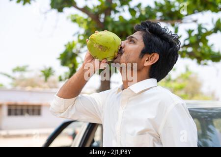 Un jeune homme assoiffé boit de l'eau de coco fraîche pendant l'été - un mélange de rafraîchissement, de vague de chaleur et de détente Banque D'Images