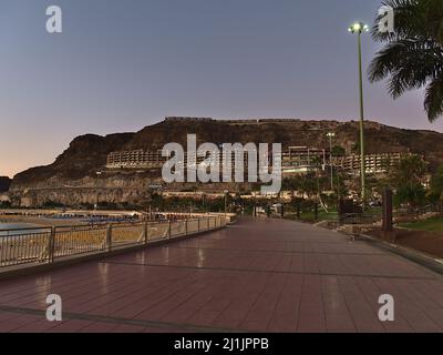 Vue sur la promenade vide de la plage populaire Playa de Amadores près de Puerto Rico, au sud de Gran Canaria, le soir avec les bâtiments de l'hôtel sur la pente. Banque D'Images