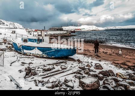 Homme avec un chien marchant près d'un vieux navire amarré par la mer à Teriberka, Russie Banque D'Images