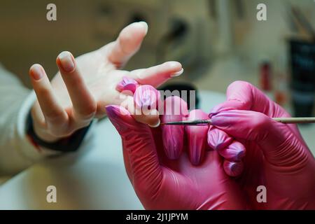 Gros plan du maître de manucure dans des gants en caoutchouc appliquant des ongles rouges dans le salon de beauté. Banque D'Images