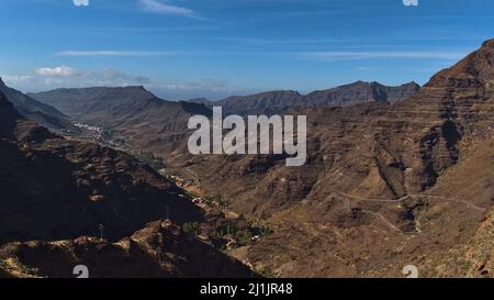 Belle vue panoramique aérienne des montagnes accidentées dans le sud de la Grande Canarie, îles Canaries, Espagne par jour ensoleillé avec ciel bleu et route sinueuse. Banque D'Images