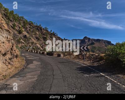 Vue sur la route rurale de montagne GC-605 dans les montagnes au nord de Mogan, Grand Canaria, îles Canaries, Espagne par temps ensoleillé en mauvais état avec des pins. Banque D'Images