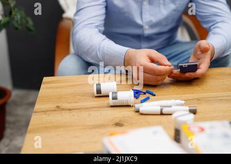 Photo rognée d'un homme assis à la table avec un ensemble de mesure du sucre pour vérifier le taux de sucre dans le sang par glucomètre, concept de diabète. Banque D'Images