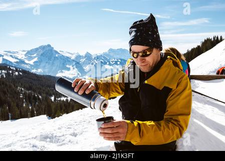 Homme versant du thé dans une thermos pendant un repos à l'Alpe Vorder Höhi avec vue sur les Alpes de Glaris avec Mürtschenstock, Glärnisch et Tödi Banque D'Images