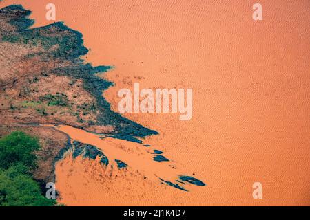 Belle vue aérienne en gros plan sur le rivage boueux et l'eau de couleur orange d'un trou d'eau dans la savane du Kenya Banque D'Images