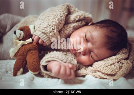 Bébé multiethnique bébé garçon dormant sur un lit. Aspect confortable avec ours en peluche Banque D'Images